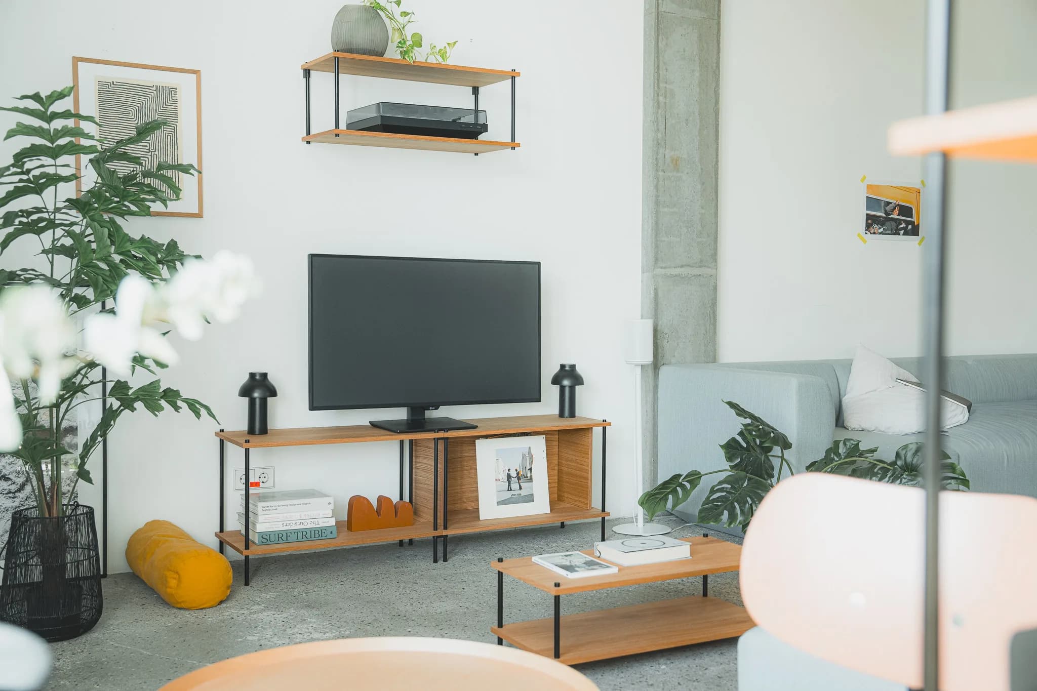 Wohnzimmer-Szene mit KUUDU-TV-Board, Couchtisch und Wandregal aus Eiche, mintgrünes Sofa, Pflanzen, Sichtbeton-Säule
