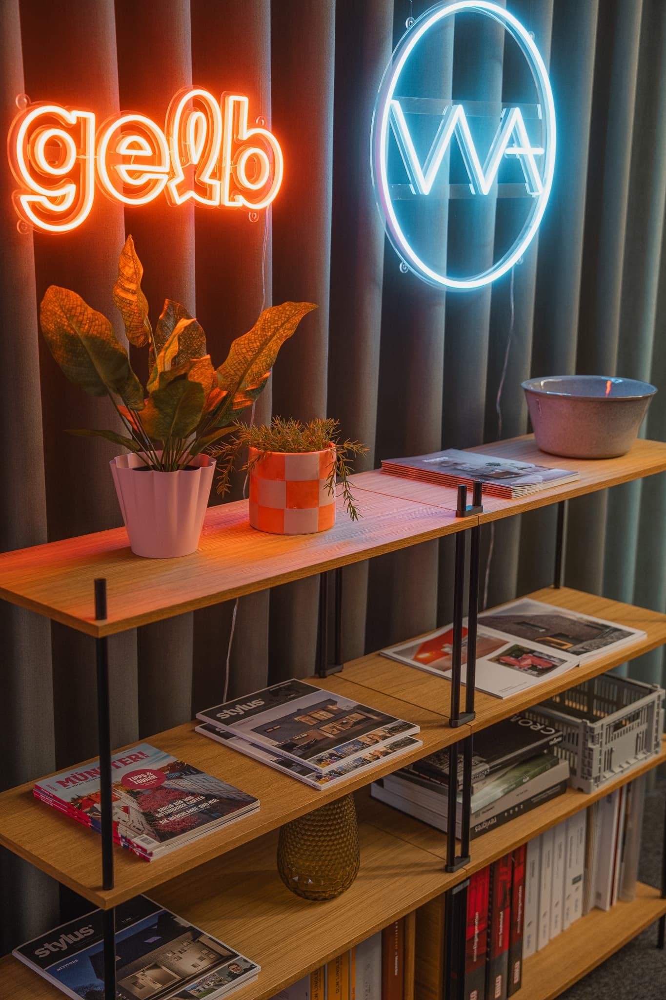 KUUDU Standregal vor Vorhang, Neon-Logos gelb und WA, Pflanzen und Magazine
